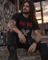 Metaleiro sentado com T-shirt Heavy Metal Força Bruta preta, calças rasgadas e botas, em cenário industrial ao pôr do sol