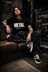 Mulher metaleira sentada com T-shirt preta Metal Se Faz Favor da Força Bruta